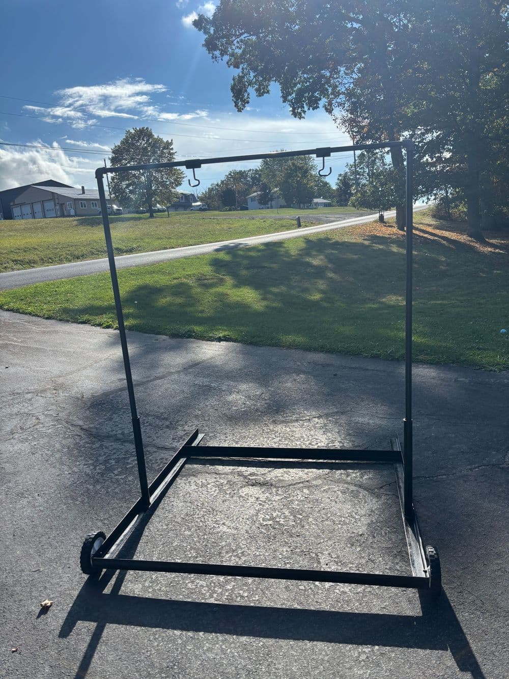 Portable black garment rack with wheels on a sunny outdoor background. Ideal for clothing display.