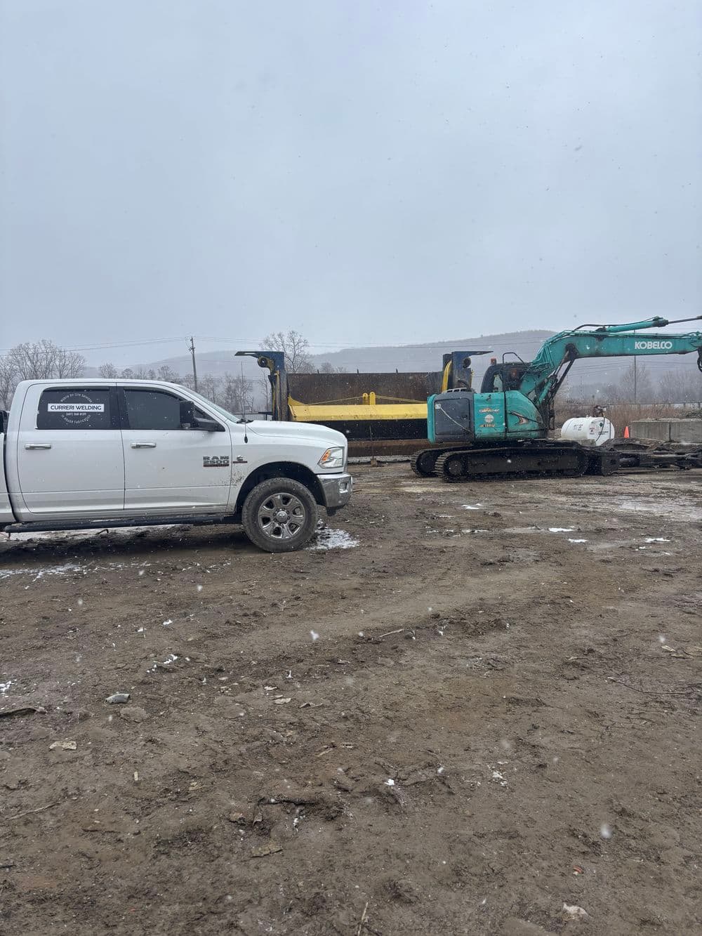 Construction site with a white truck and green excavator on a snowy day.