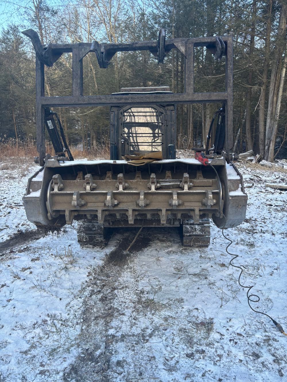 Snow-covered forestry machine with tracks, forest backdrop, ready for land clearing operations.