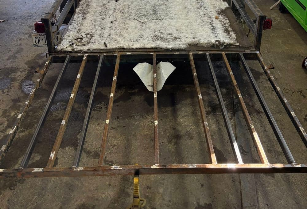 Rusty metal trailer frame with snow covering the bed, set in a workshop environment.